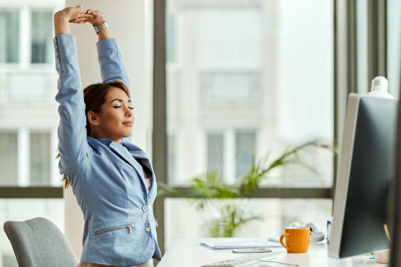 Smiling businesswoman with raised arms stretching at office desk