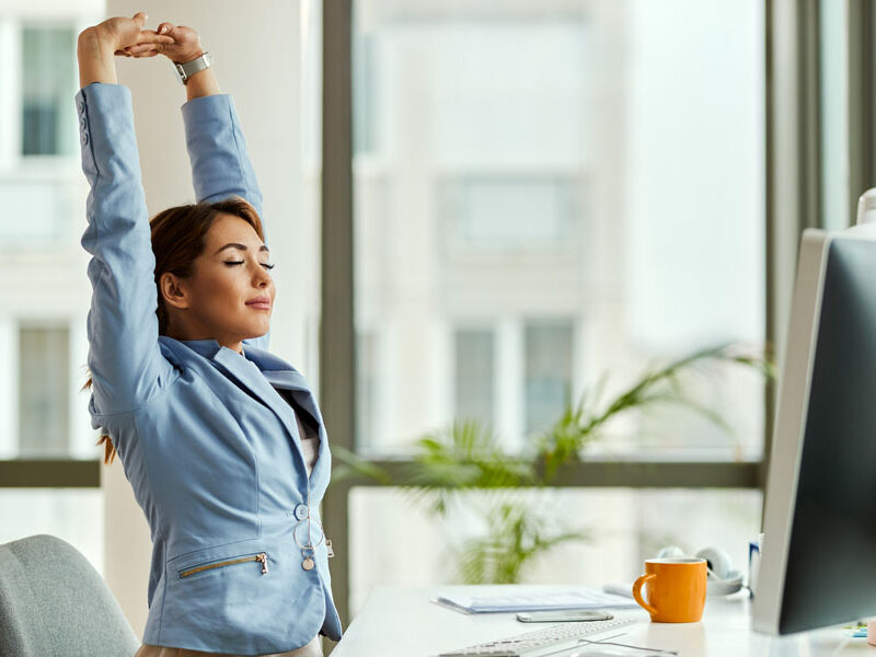 Smiling businesswoman with raised arms stretching at office desk